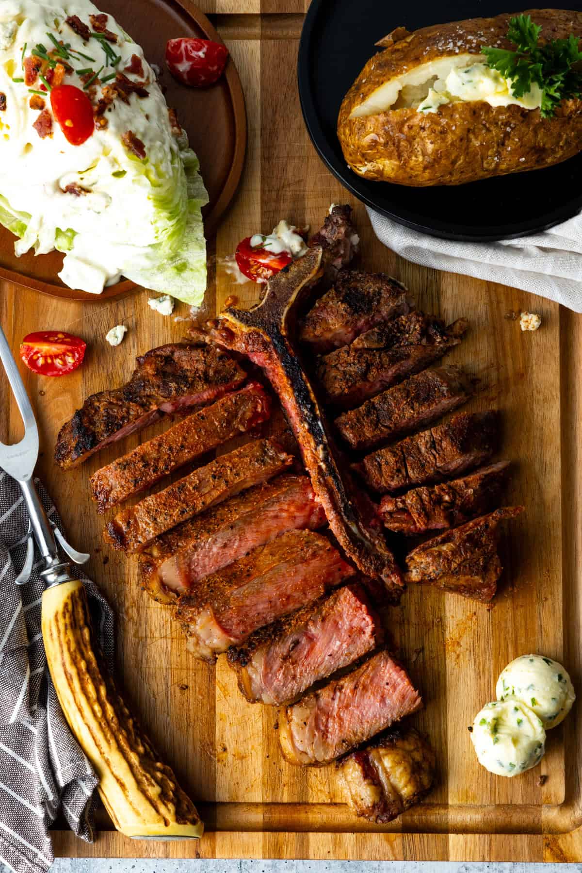 Steak sliced in pieces with baked potato and wedge salad on wood cutting board.