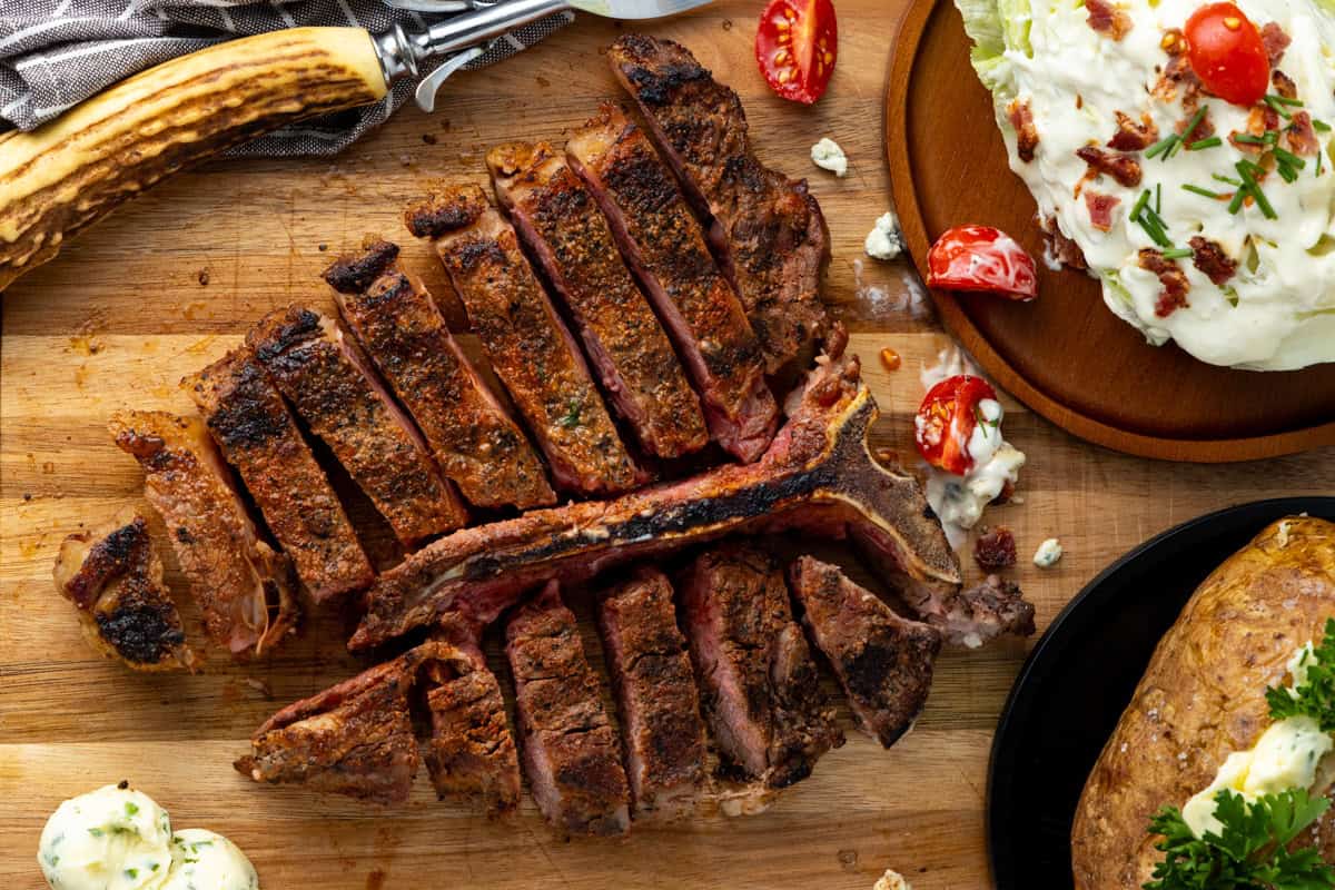 Sliced steak on cutting board with side dishes on potato and salad.