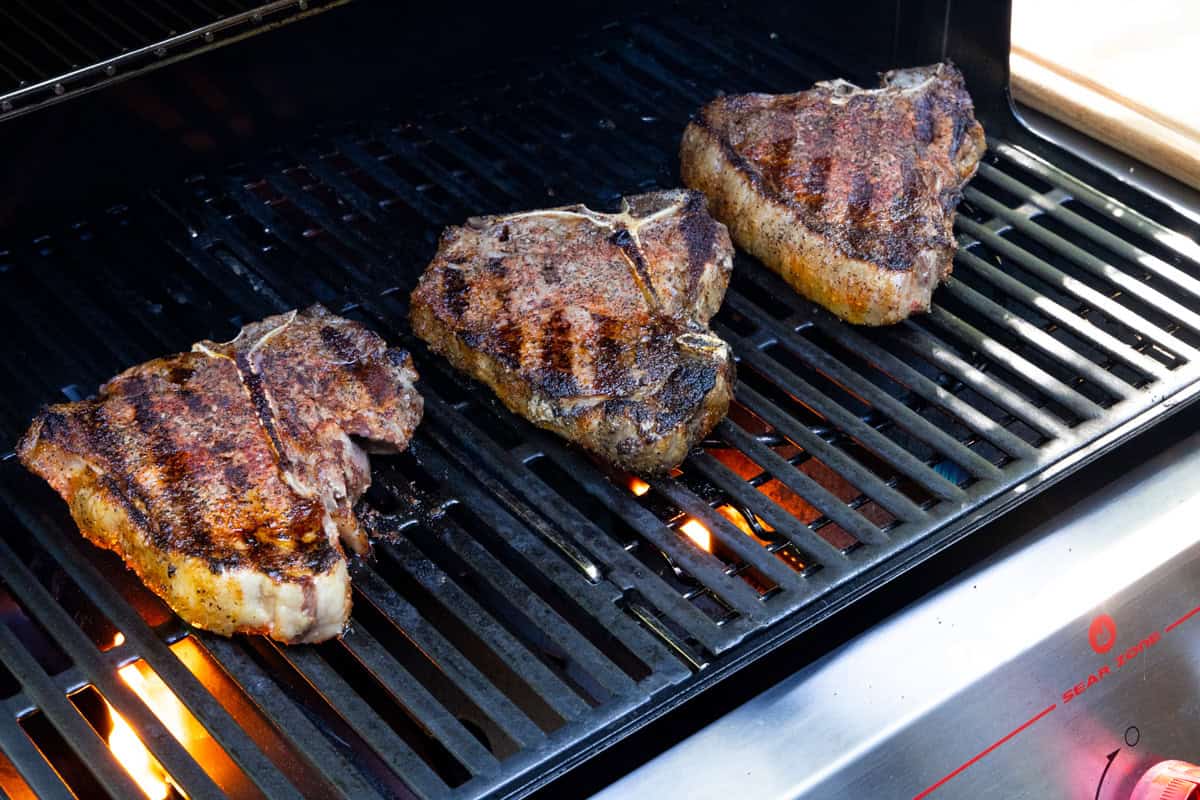 Three t bone steaks on grill cooking.