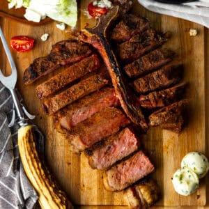 Grilled t bone steak sliced on cutting board with side salad and butter.