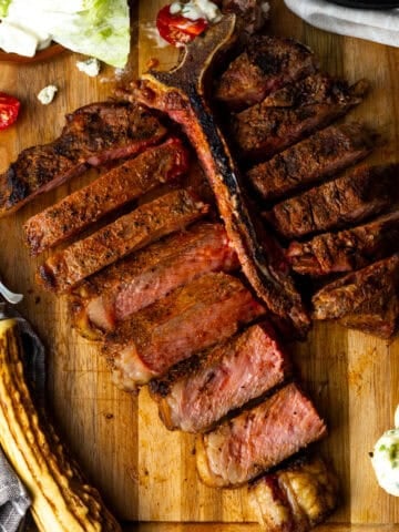 Grilled t bone steak sliced on cutting board with side salad and butter.